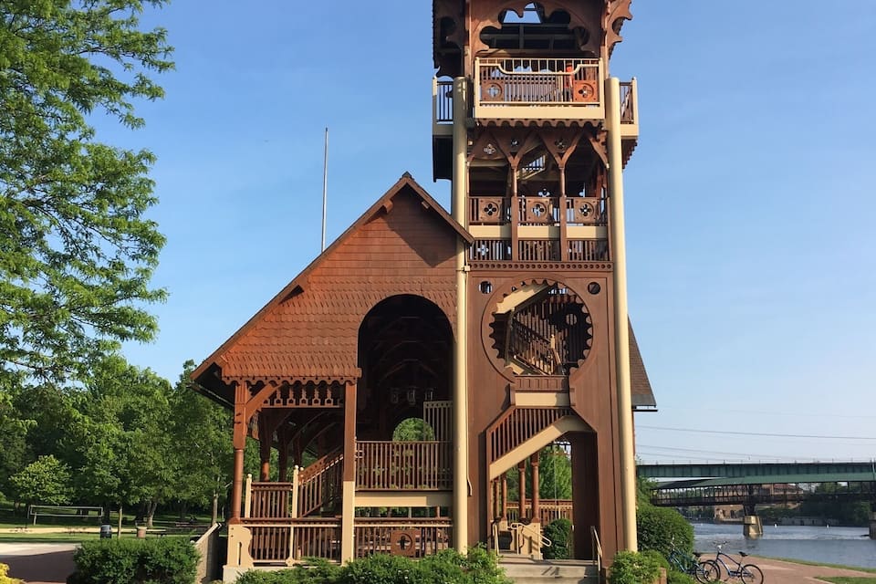 A clock tower with a balcony and a bridge in the background.