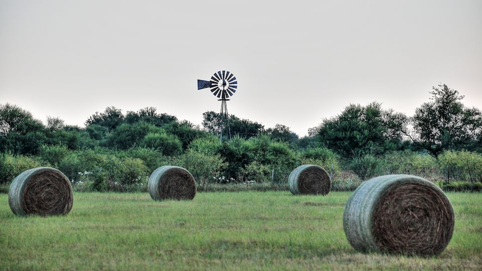 A windmill and hay bales in a field.