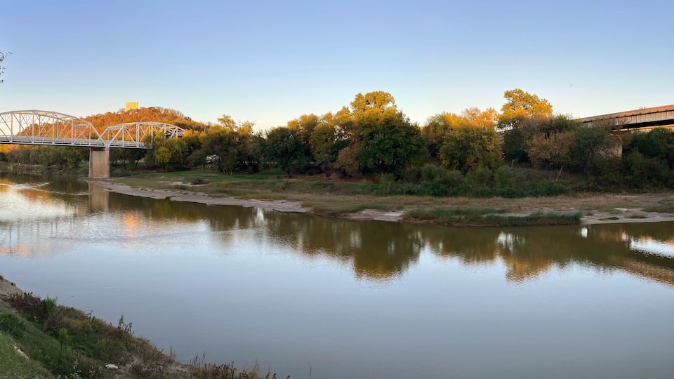 A river with a bridge, trees, and a clear sky.