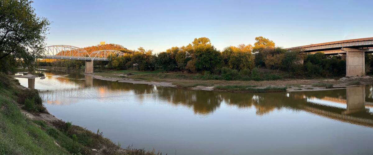 A river with a bridge, trees, and a clear sky.