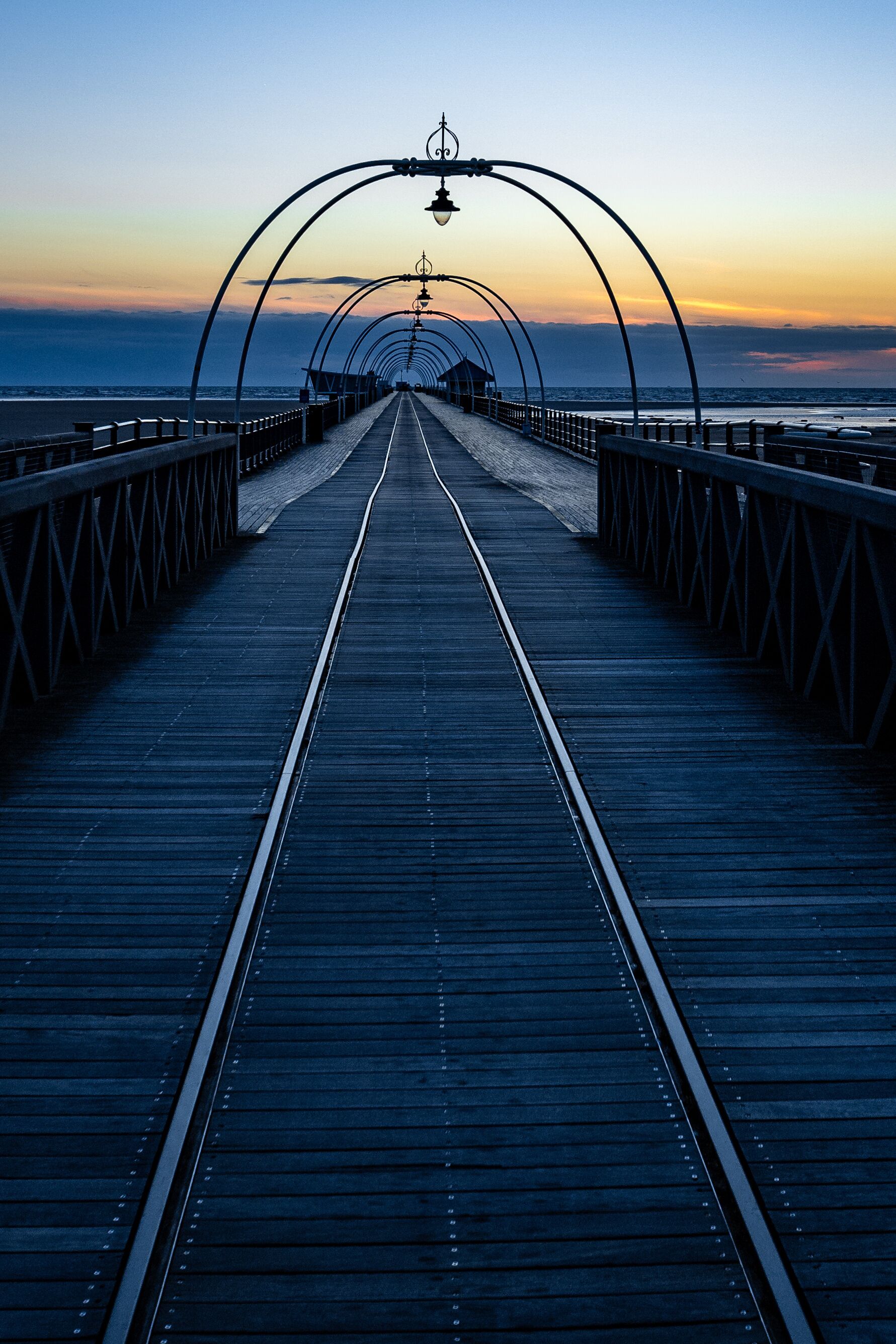 Long, narrow Southport Pier stretching across the beach at sunset