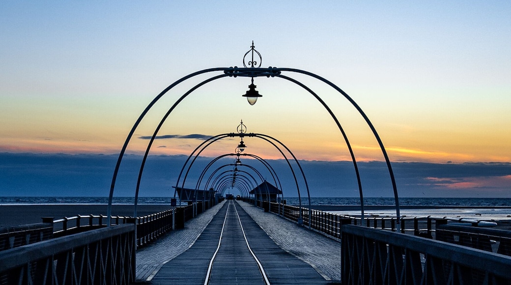 Long, narrow Southport Pier stretching across the beach at sunset