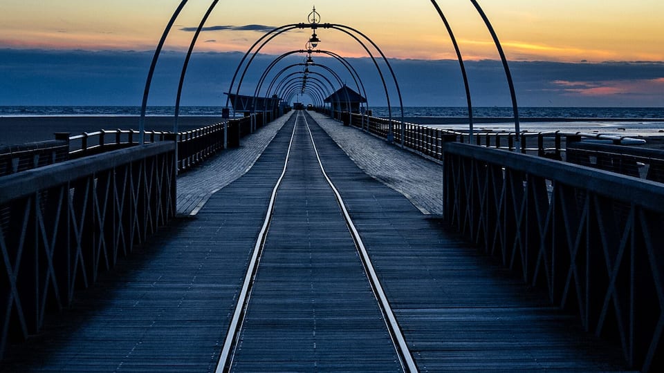 A wooden boardwalk leading to a beach with metal arches overhead.