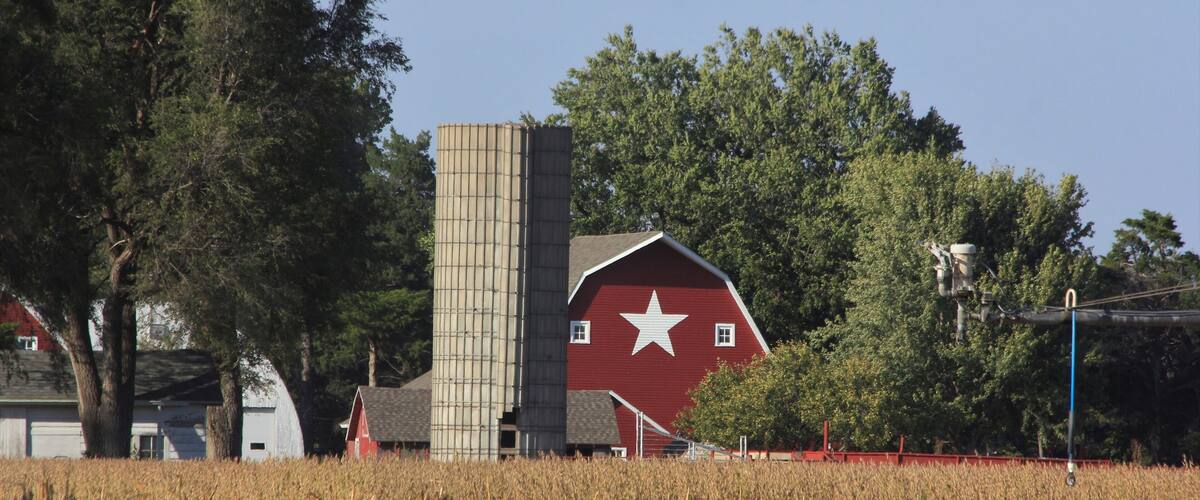 A red barn with a white star, a silo, and a cornfield.