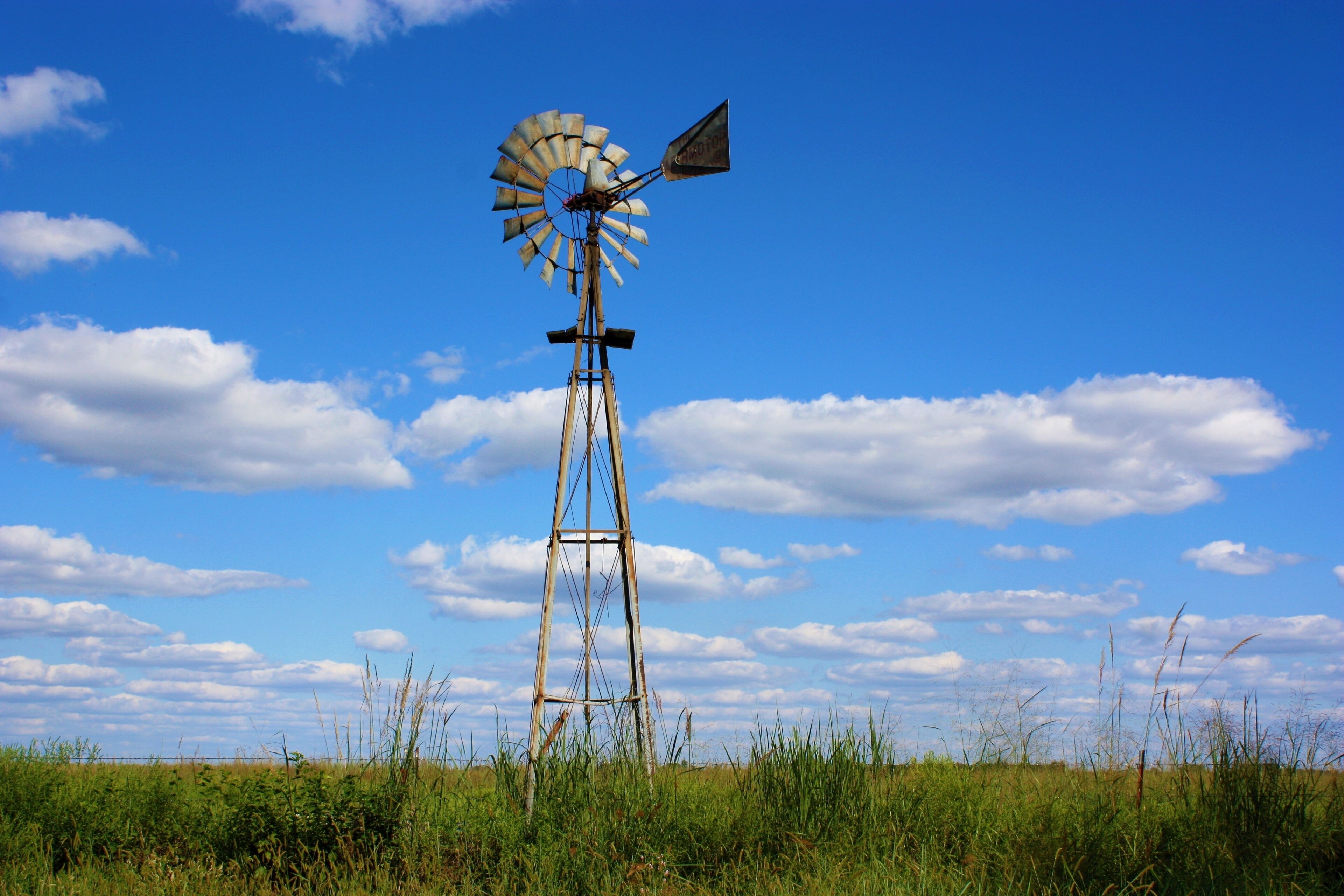windmill in the field in Kansas west of Sterling Kansas with grass,blue sky, and white clouds.