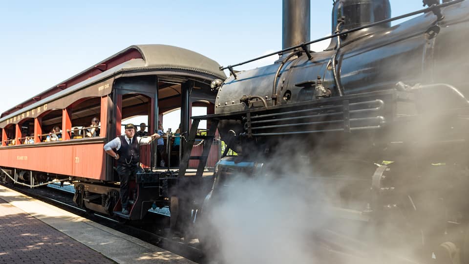 A steam locomotive pulling a red passenger car at a station.