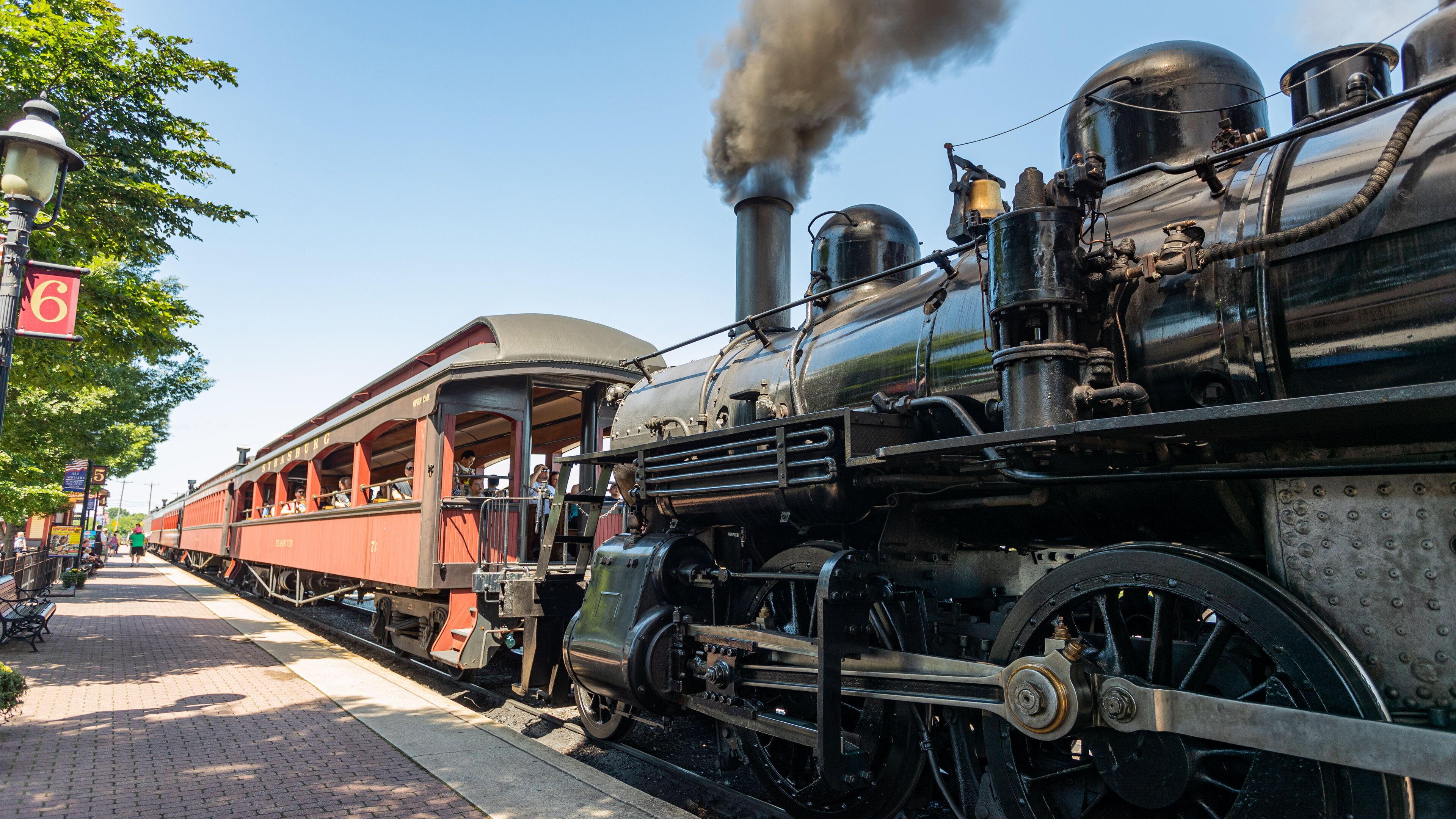 A steam locomotive with passengers on board, emitting steam, at a train station.