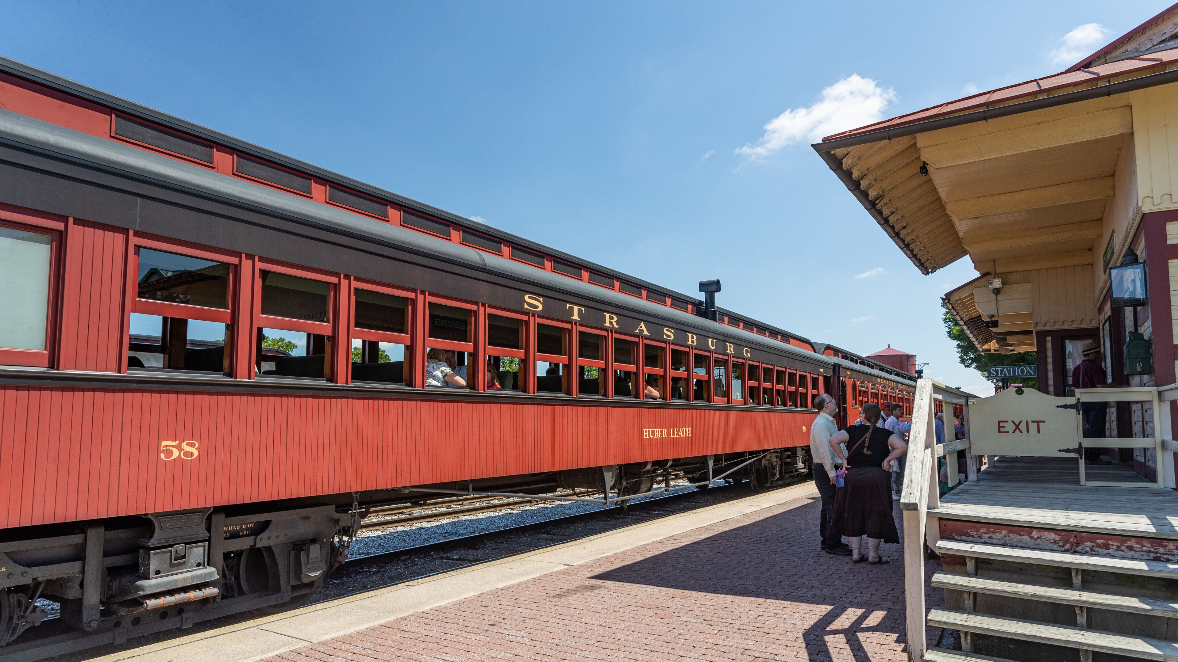 A red train with 'STRASBURG' written on the side, stopped at a station with a platform and an 'EXIT' sign.