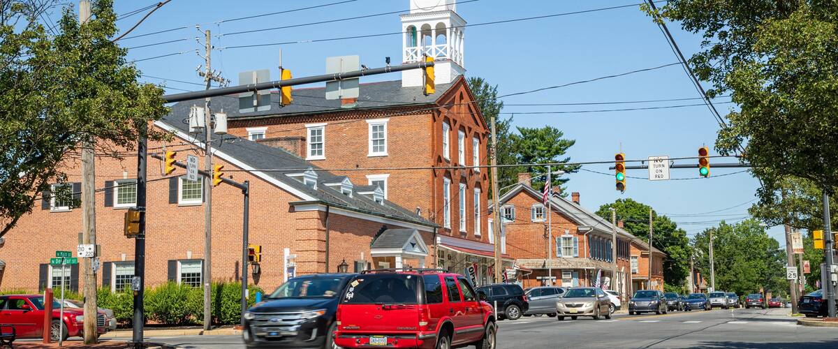 A street with brick buildings, a church with a clock tower, and cars driving.