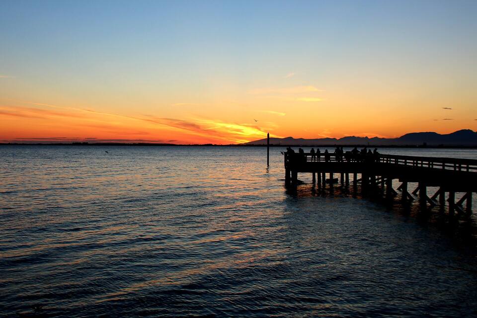 A sunset over a calm sea with a pier extending into the water.