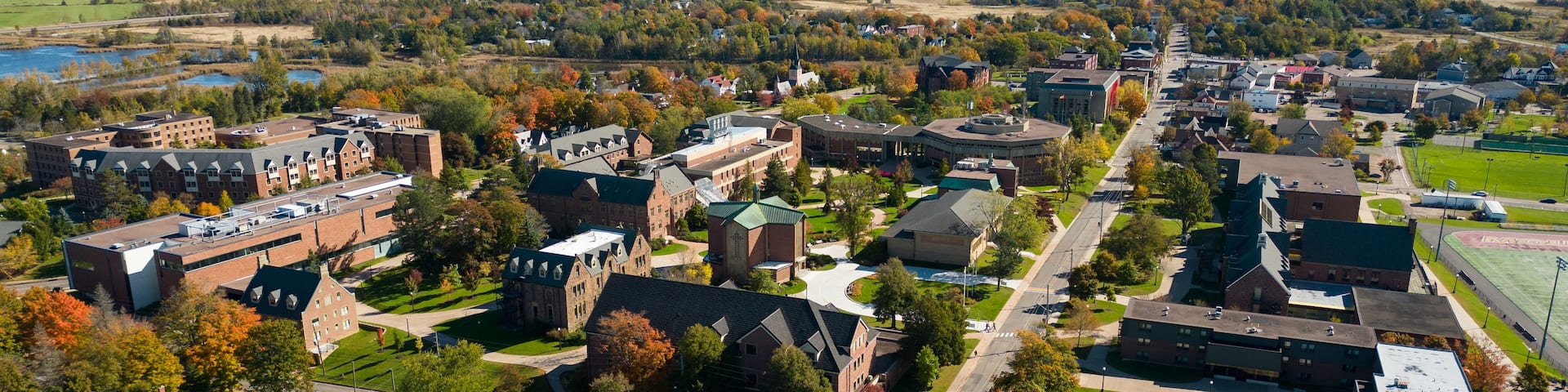 An aerial view of a town with a mix of residential and institutional buildings, a church, and a large open field in the distance.