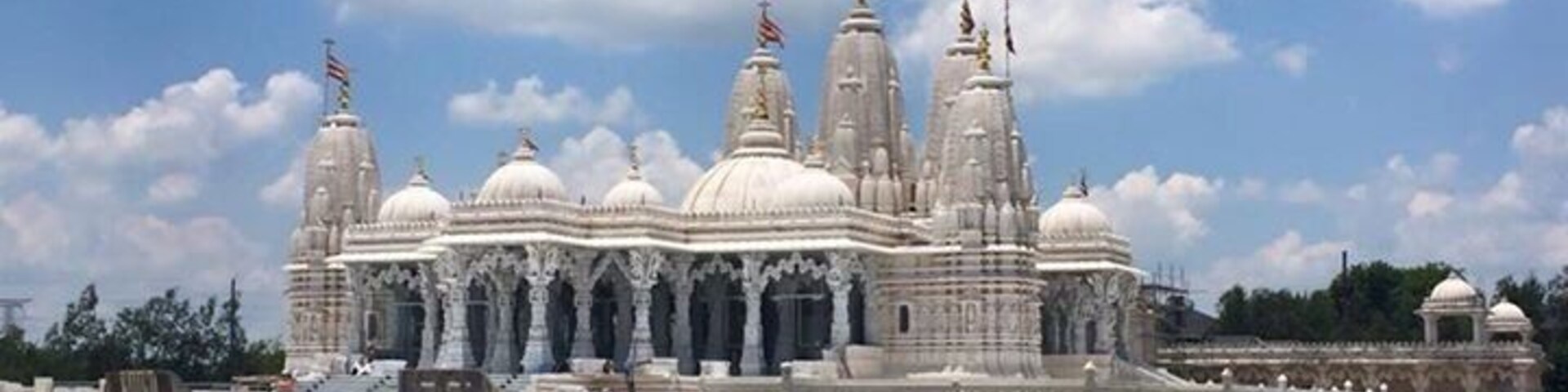 Um templo grande e branco, com várias cúpulas e torres, rodeado por um jardim bem cuidado.