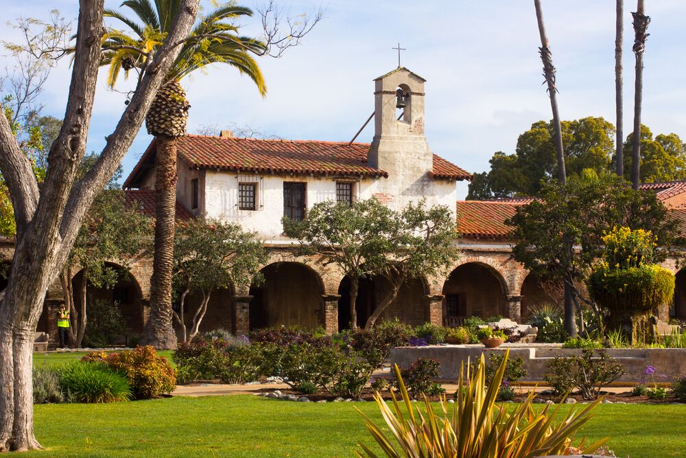 A historic building with a bell tower, surrounded by palm trees and a well-maintained garden.