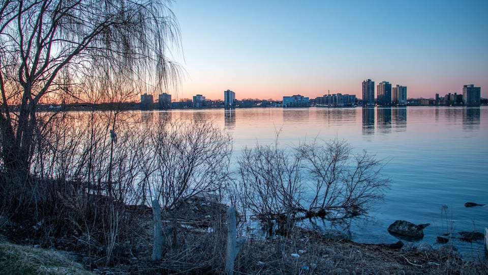 A calm river reflecting city buildings at dusk.