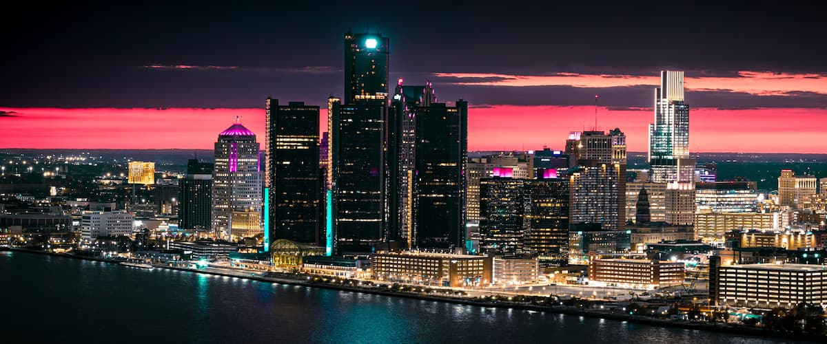 A city skyline at dusk with illuminated buildings and a river in the foreground.