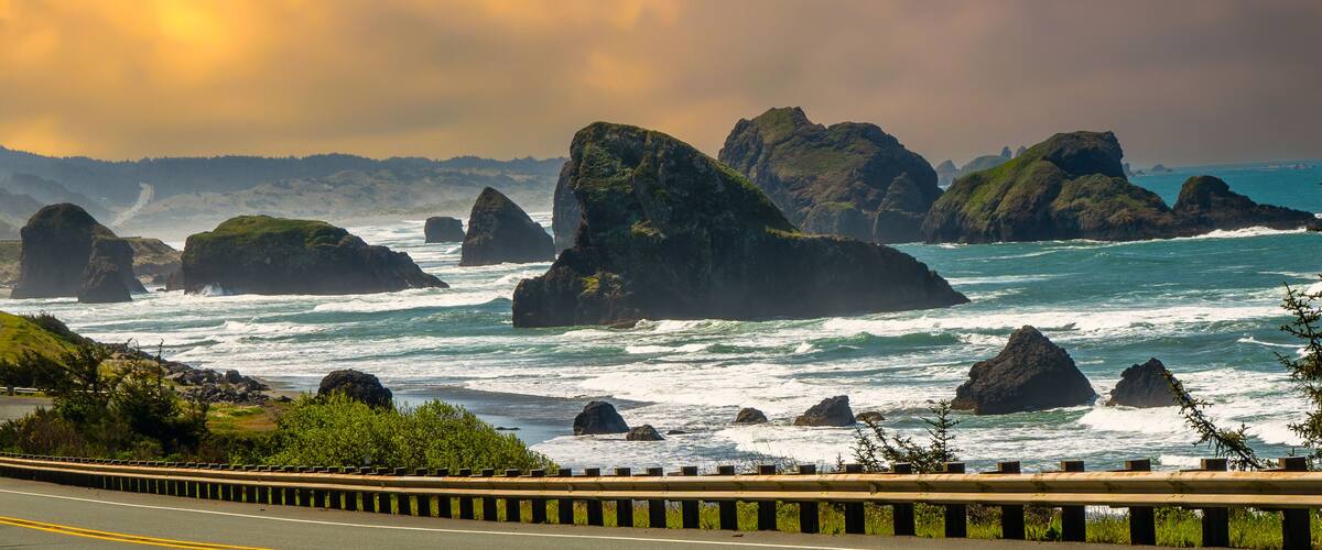 A coastal road with a truck, surrounded by rugged cliffs and waves.