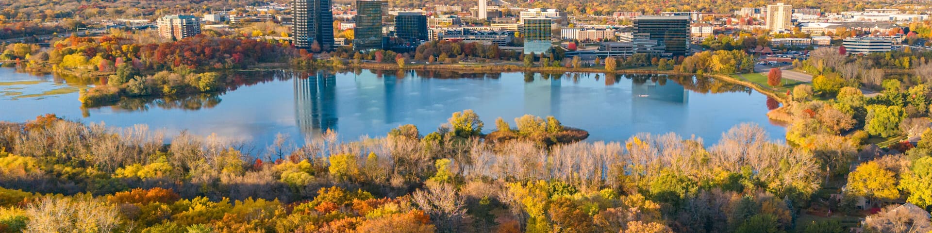 A cityscape with autumn foliage, a lake, and modern buildings.