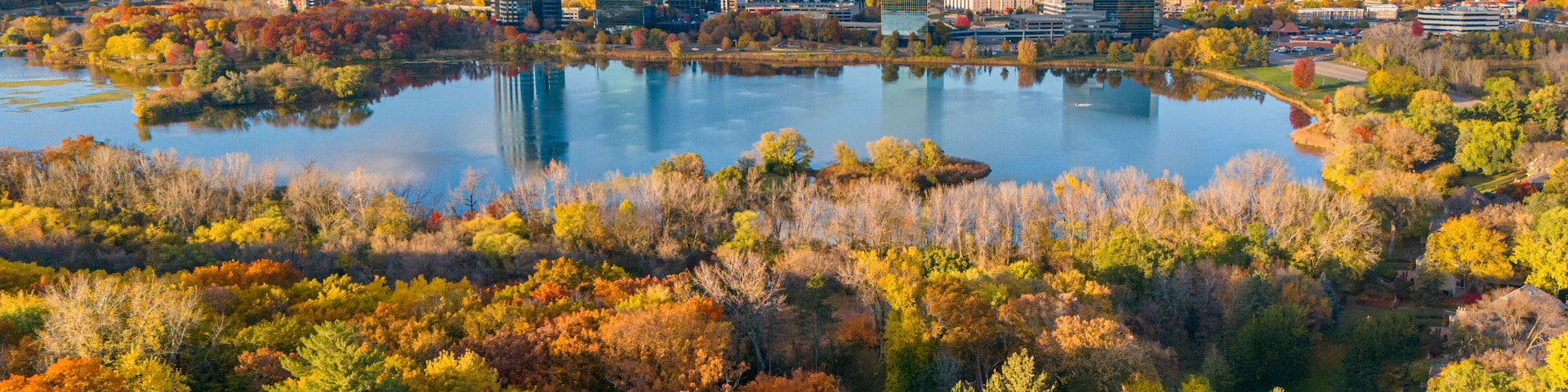 Paisaje urbano con follaje otoñal, un lago y edificios modernos.
