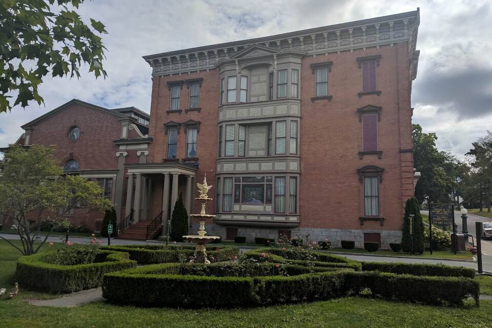 A historic brick building with a fountain in the front garden.