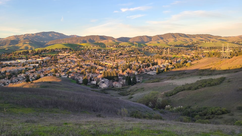 A town nestled in a valley with rolling hills and mountains in the background.