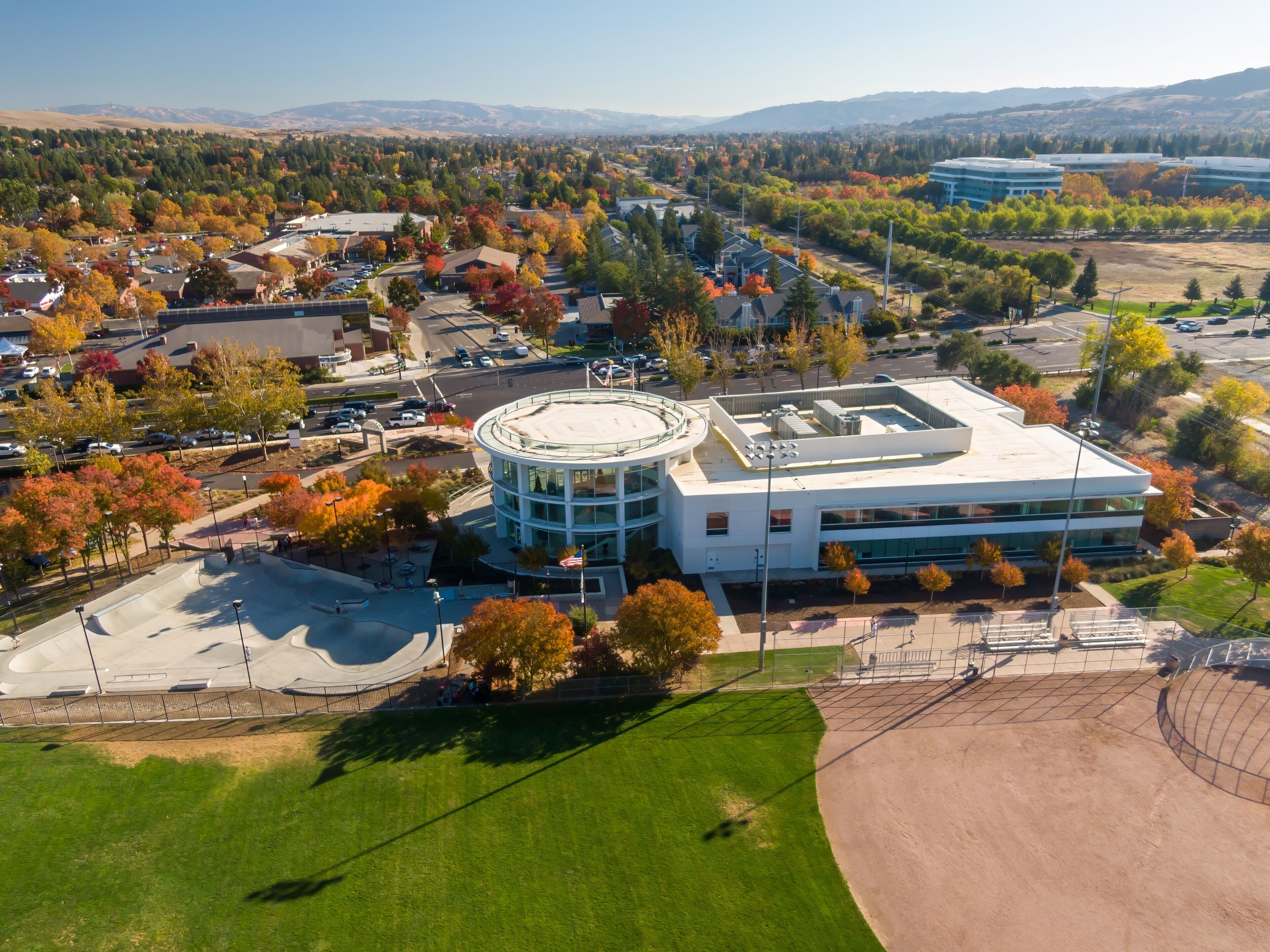 Aerial view of San Ramon City Hall, San Ramon, California, USA during autumn. The photo captures the colorful foliage, a modern building, and a baseball field.