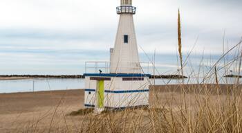 A lighthouse on a sandy beach with a calm body of water in the background.