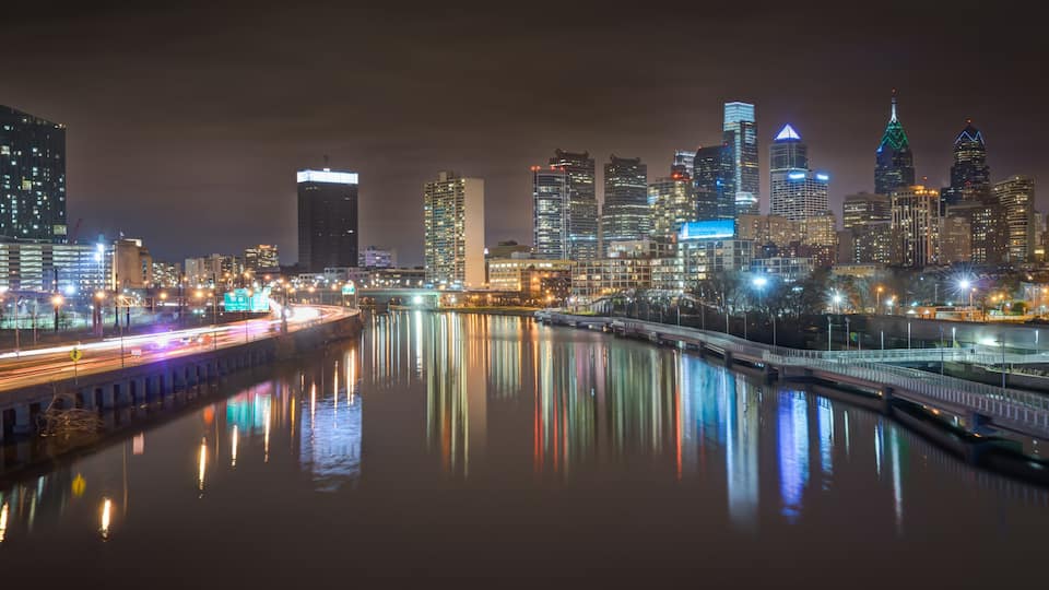 A nighttime cityscape with illuminated skyscrapers and a river reflecting lights.