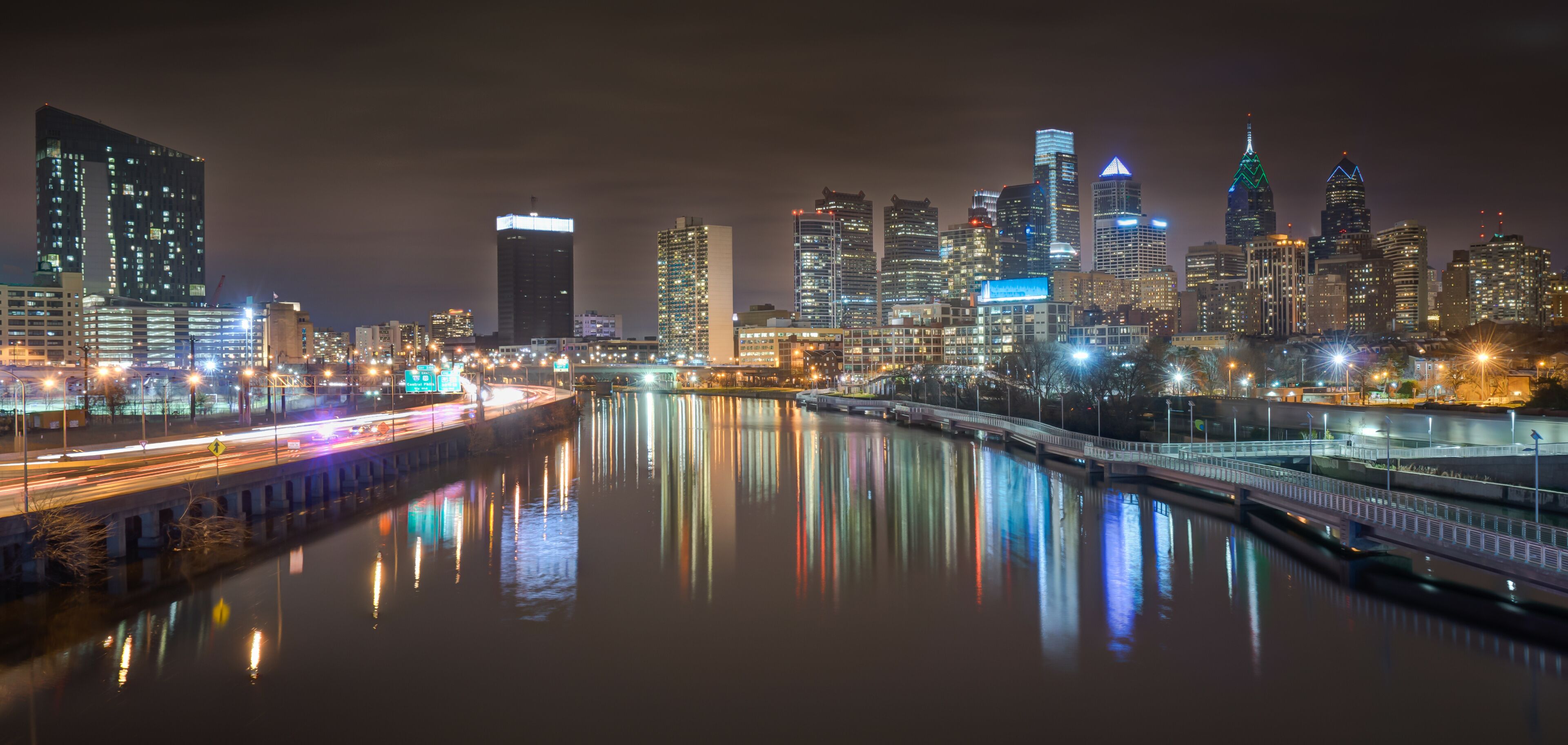 A nighttime cityscape with illuminated skyscrapers and a river reflecting lights.