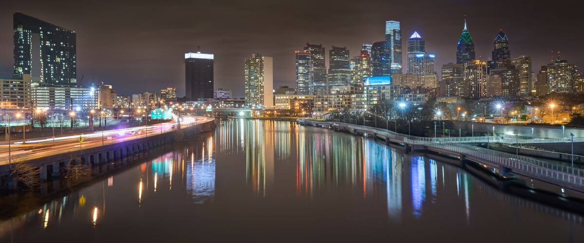 A nighttime cityscape with illuminated skyscrapers and a river reflecting lights.