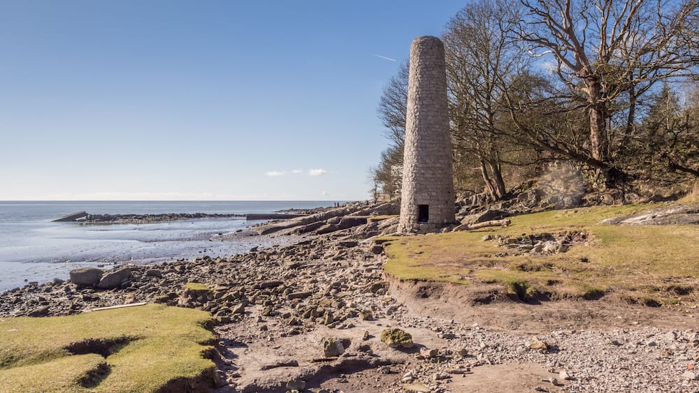 A coastal landscape with a stone tower, rocky beach, and a clear sky.