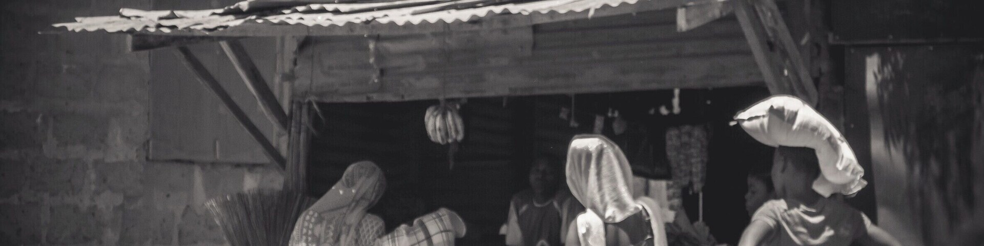 Um grupo de pessoas vestindo trajes típicos em frente a uma construção rústica com telhado de chapa metálica.