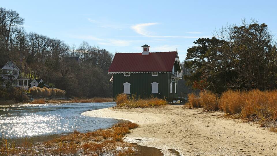 A riverbank with a house, trees, and a sandy path.