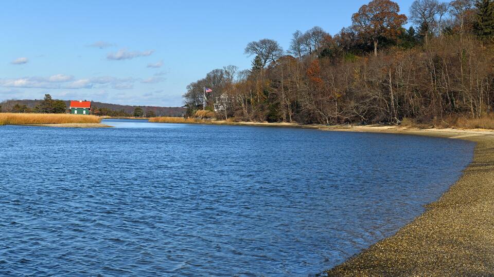 A calm lake with a red house on the left and a forested hill in the background.