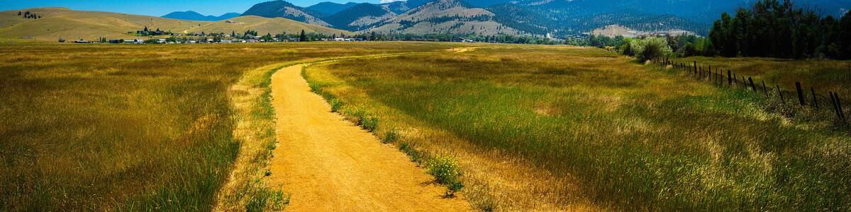 Tranquil rural dirt road curving through the prairie toward Lolo National Forest in Helena, Montana