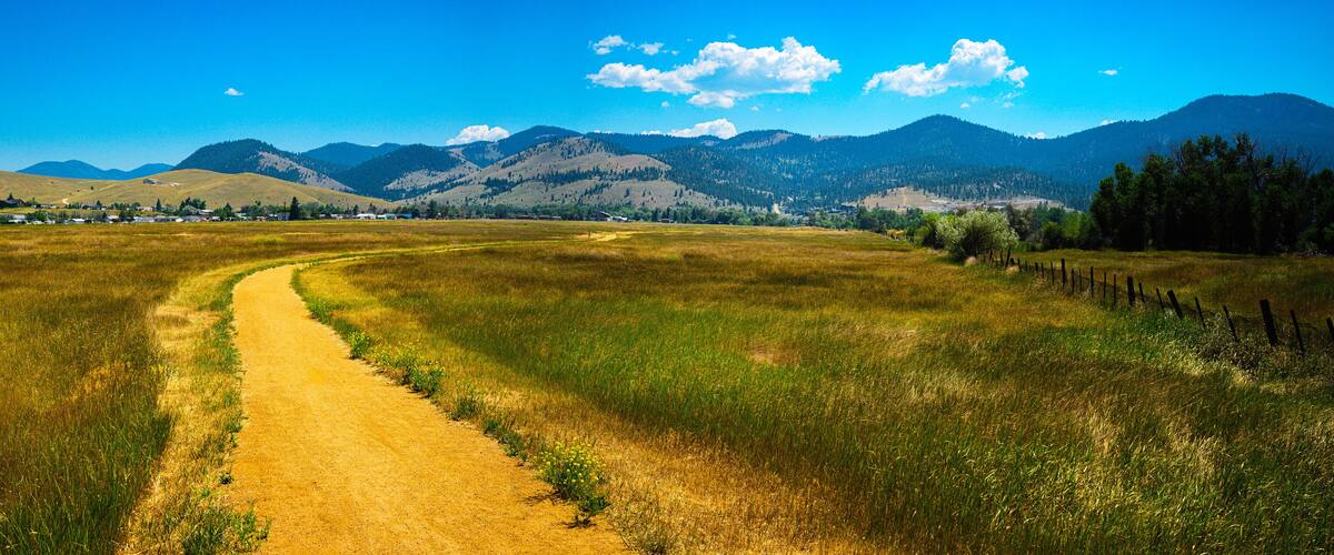 Tranquil rural dirt road curving through the prairie toward Lolo National Forest in Helena, Montana