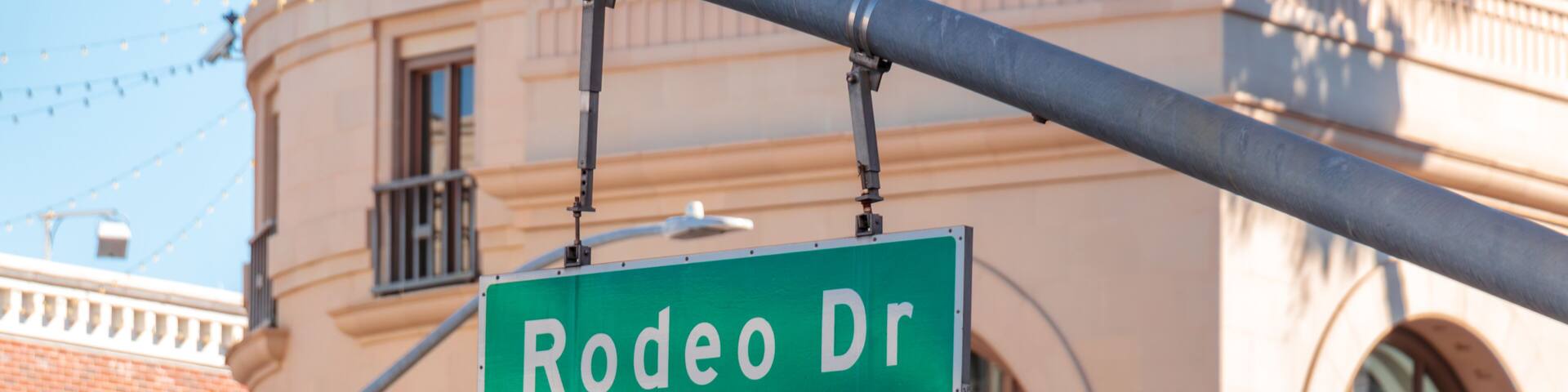 Close-up view of the Rodeo Drive street sign suspended above the street with upscale architecture in the background in Beverly Hills, California, USA. Luxury shopping district, city landmark