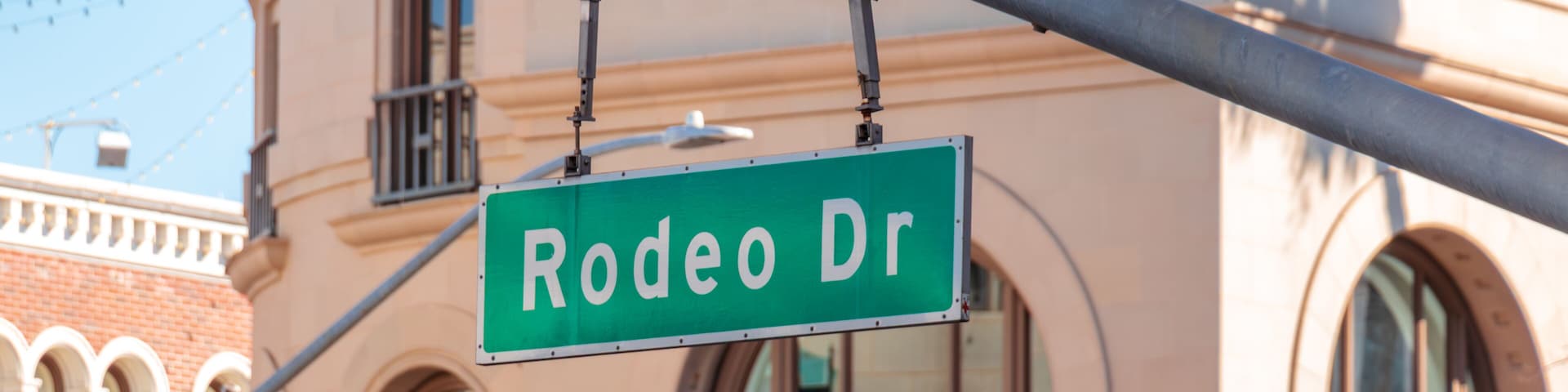 Close-up view of the Rodeo Drive street sign suspended above the street with upscale architecture in the background in Beverly Hills, California, USA. Luxury shopping district, city landmark