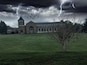 A building with a tower, surrounded by a grassy field and a bare tree.