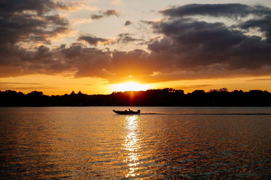 Beautiful sky and lake with boats, people relaxing on the shore at sunset. Beautiful orange and blue sky at dawn. Lake Bowen Anchor Park, Inman, SC, USA