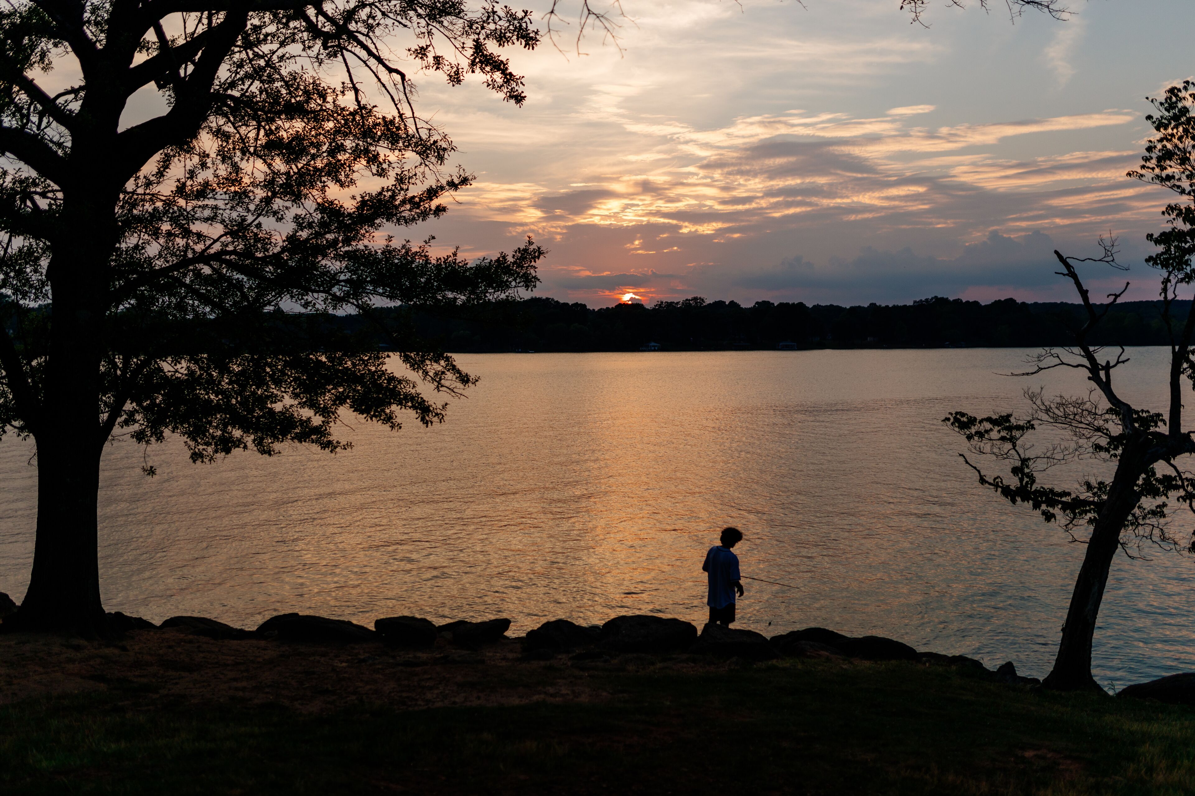 Beautiful sky and lake with boats, people relaxing on the shore at sunset. Beautiful orange and blue sky at dawn. Lake Bowen Anchor Park, Inman, SC, USA 