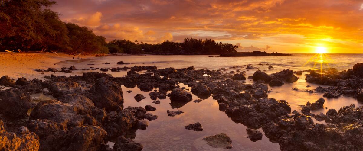 A rocky shoreline with a sunset over the ocean.