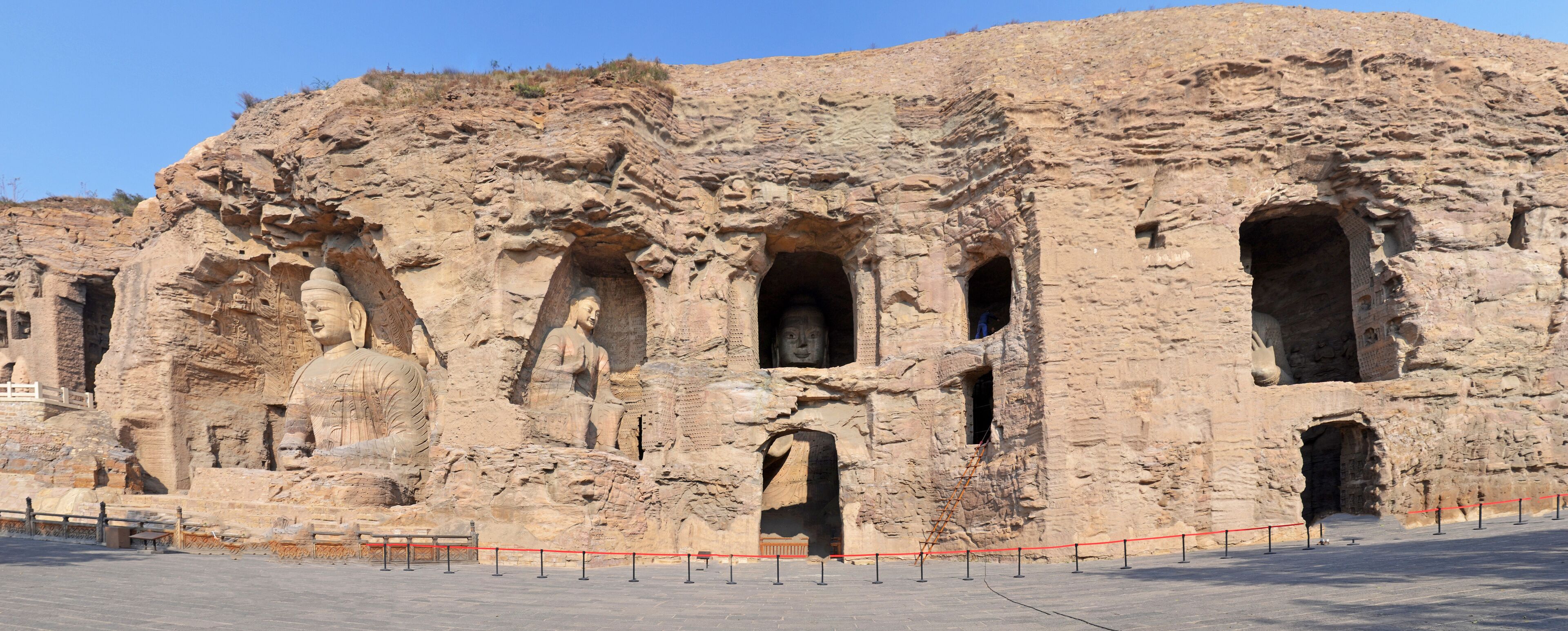 A large rock face with carved Buddha statues and multiple openings.