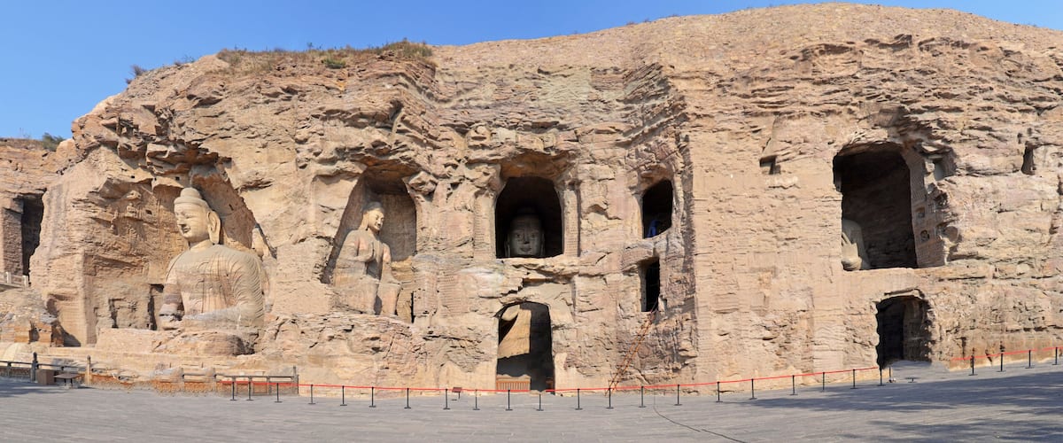 A large rock face with carved Buddha statues and multiple openings.