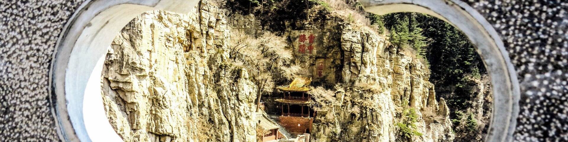 A stone structure with a carved window reflecting a mountainous landscape and traditional architecture.