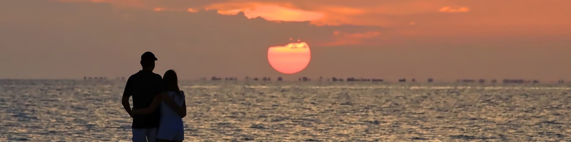 Beach lovers watch the sunset over Sanibel Island from Fort Myers Beach, Florida, USA.