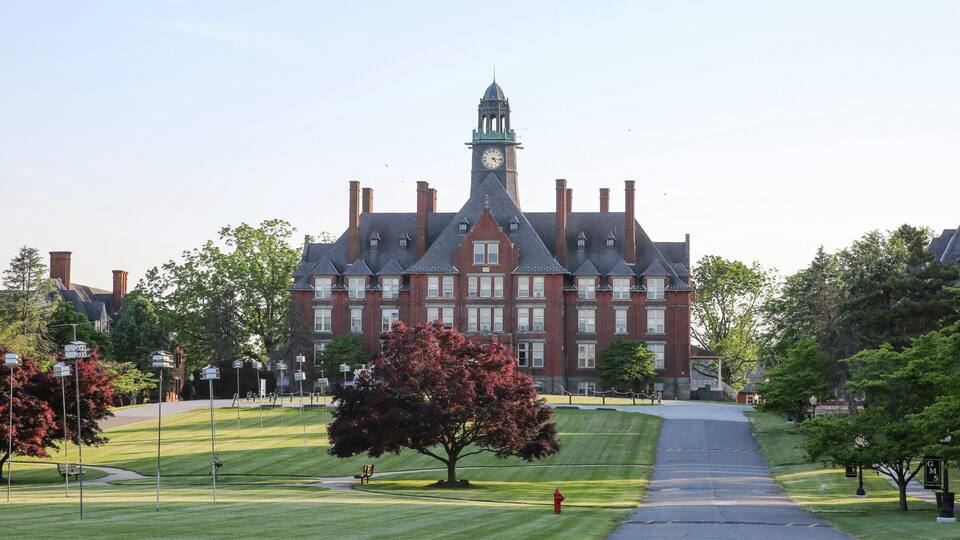 A large red brick building with a clock tower, surrounded by green lawns and trees.