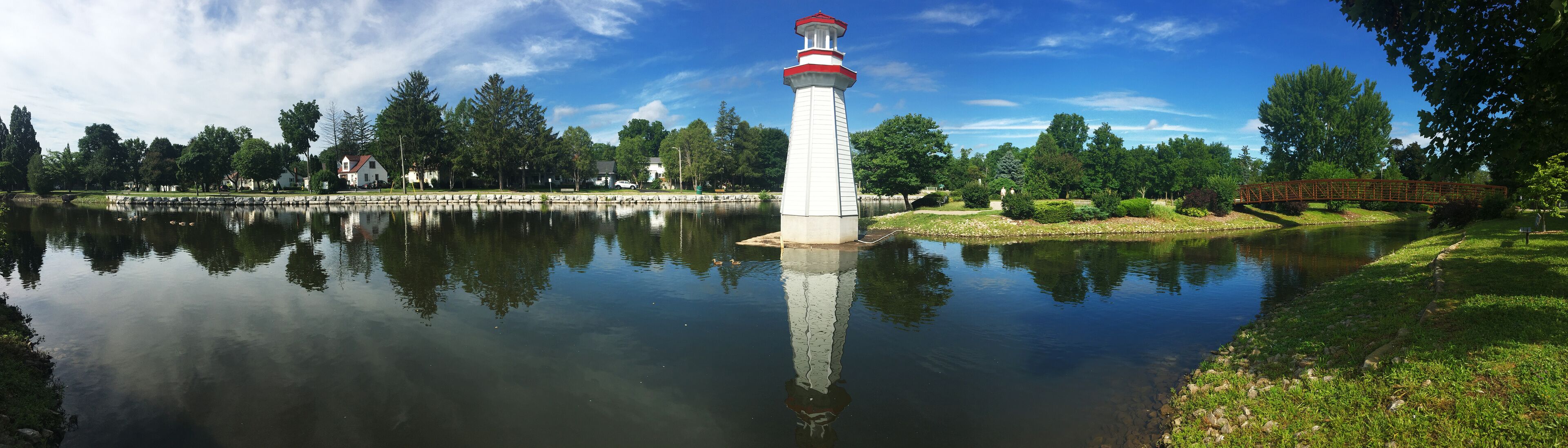 A lighthouse by a calm lake with a bridge in the background.