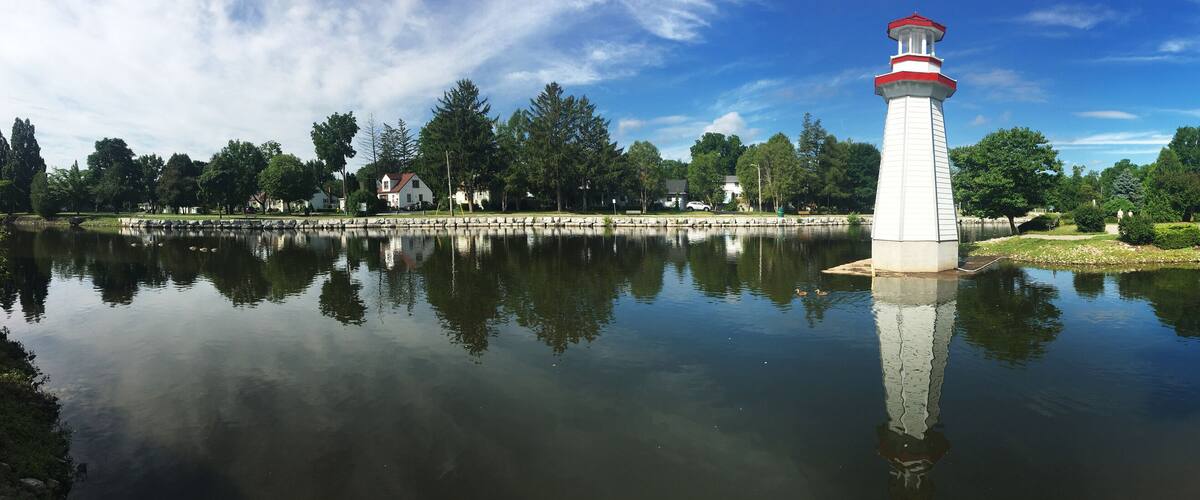 A lighthouse by a calm lake with a bridge in the background.