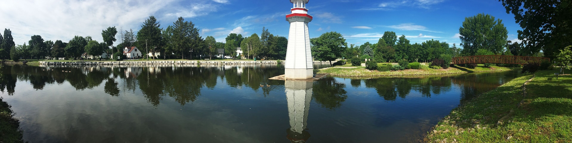 A lighthouse by a calm lake with a bridge in the background.