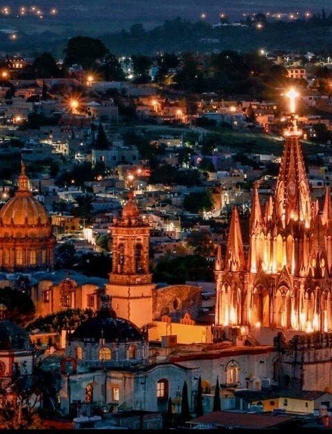 Eine beleuchtete Stadtlandschaft bei Nacht mit Gebäuden, einem markanten Dom mit aufwendigen Türmen und einer Kuppelstruktur.
